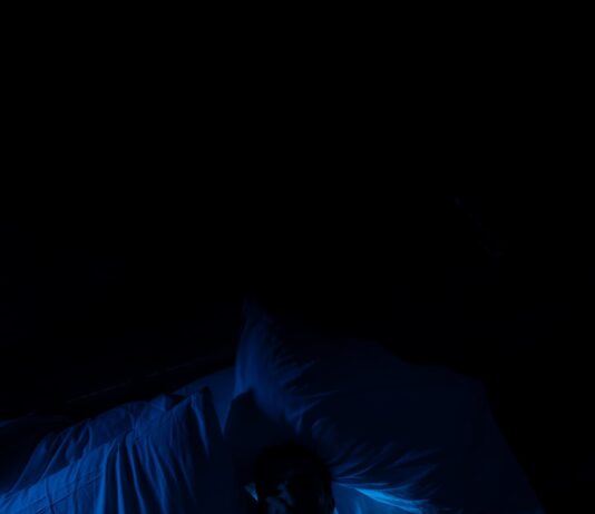 “10분만 더 누워있을까?” 아침 피로의 진짜 원인, ‘수면 빚’ 때문입니다 A person laying in a bed in a dark room